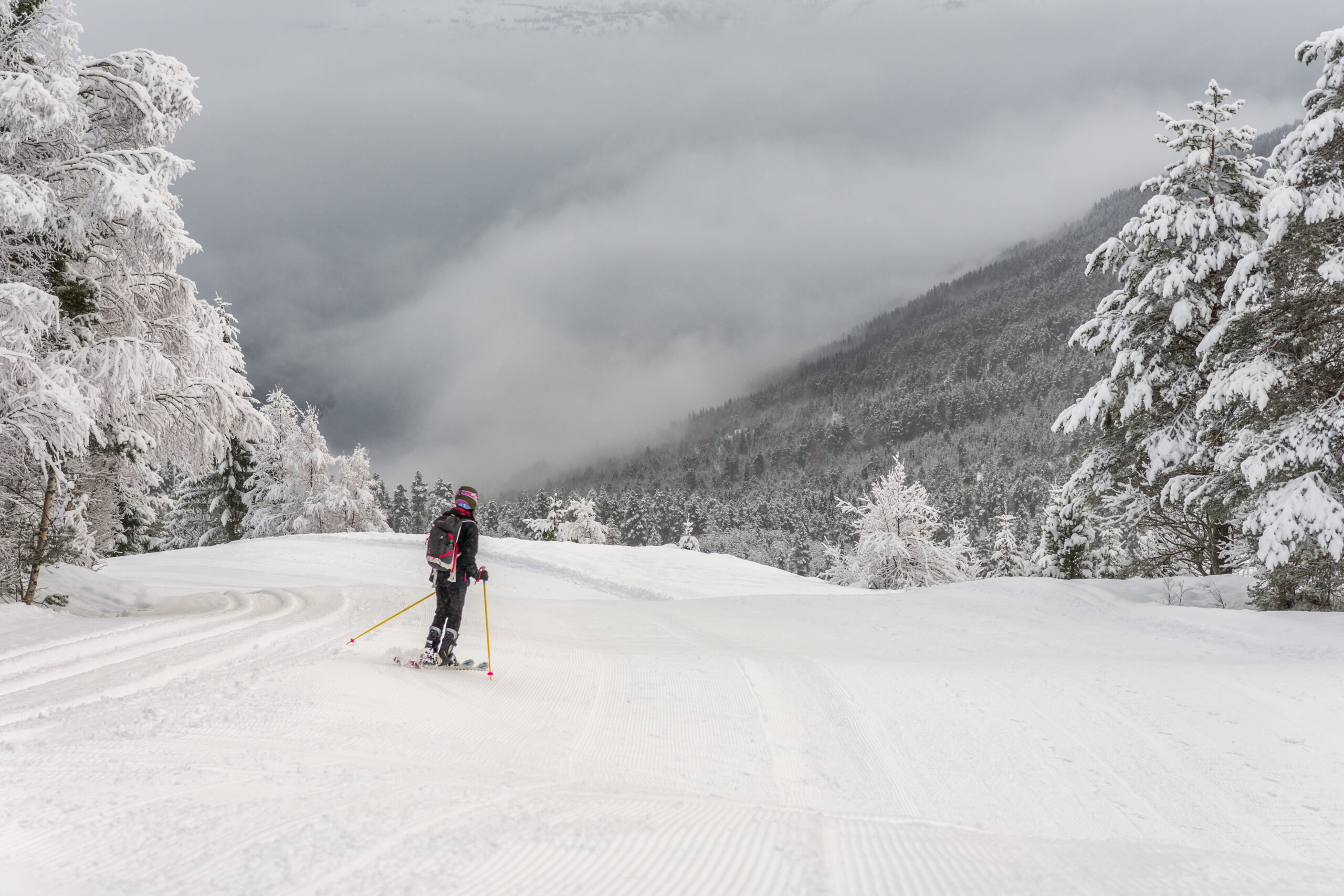 Kvinne i svart skiantrekk med hjelm og ryggsekk kjører ned over det snøkledde fjellet i skisenteret i Stryn.
