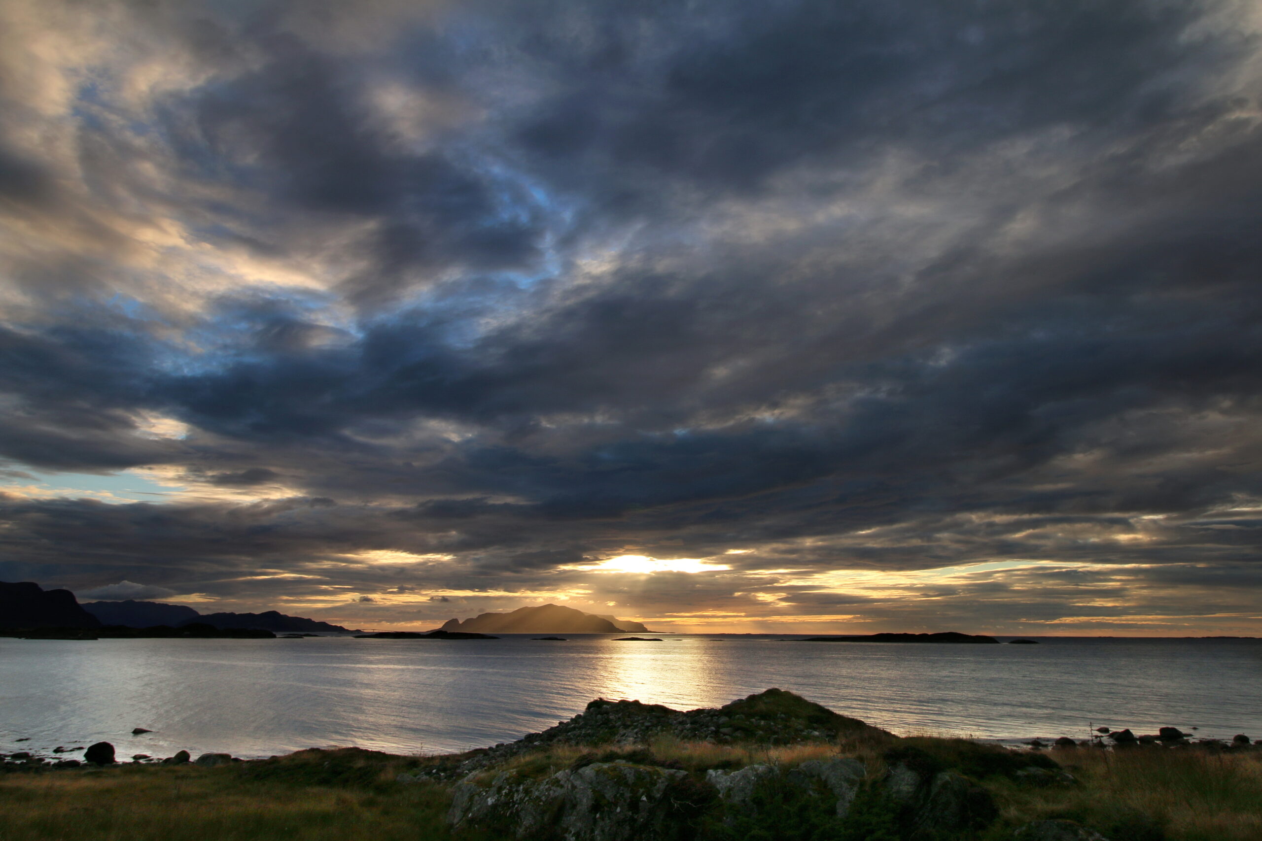 Utsikt fra Flø mot øya Runde ved solnedgang, med varme farger på himmelen og havet i bakgrunnen.