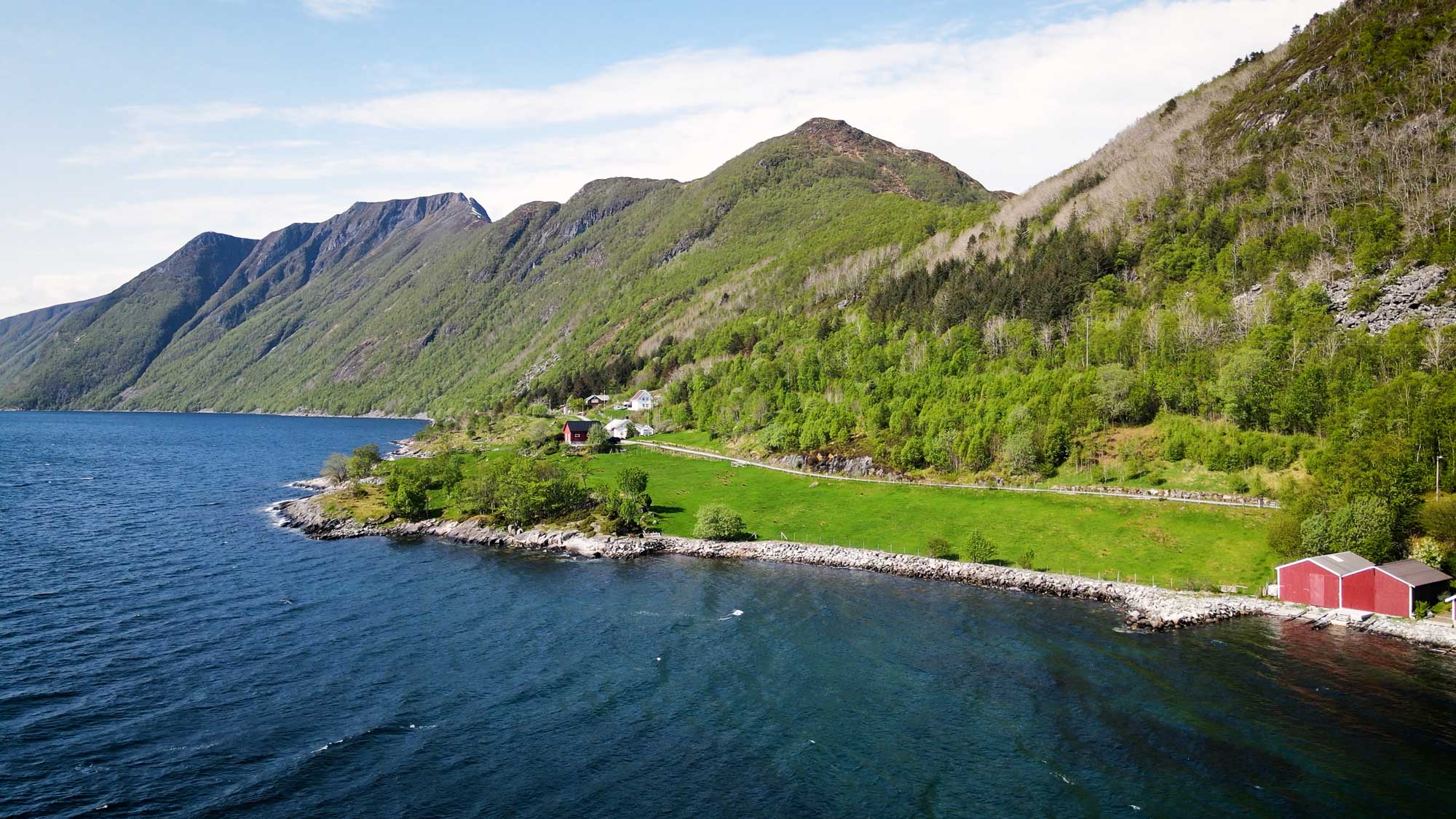 Bilde av Almestranda med sjø i forgrunnen og landskap i bakgrunnen.