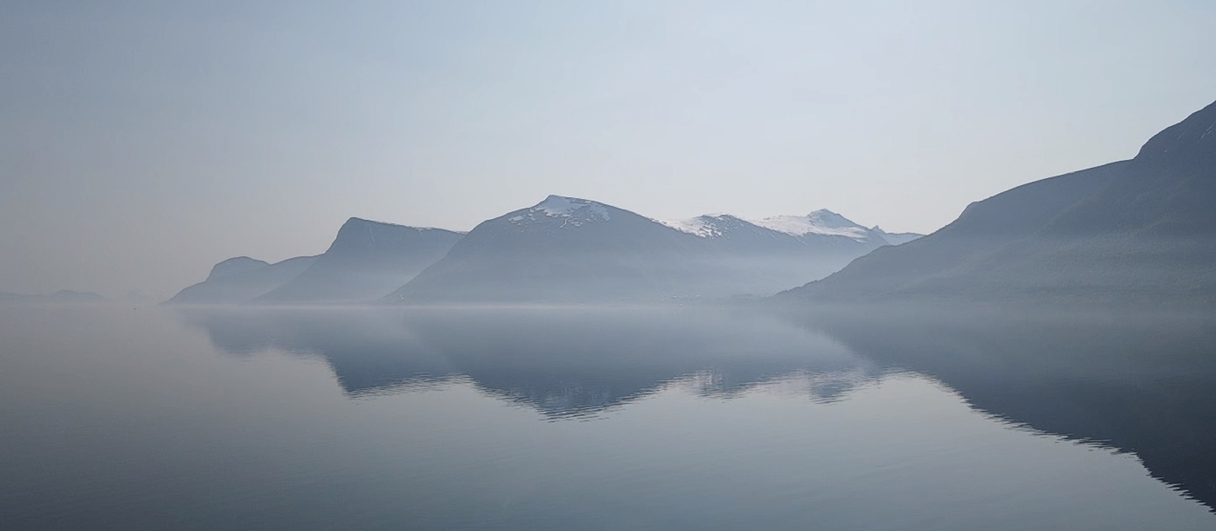 Oversiktsbilde av Almestranda i mykt morgenlys, med lett dis over området og fjorden i bakgrunnen.