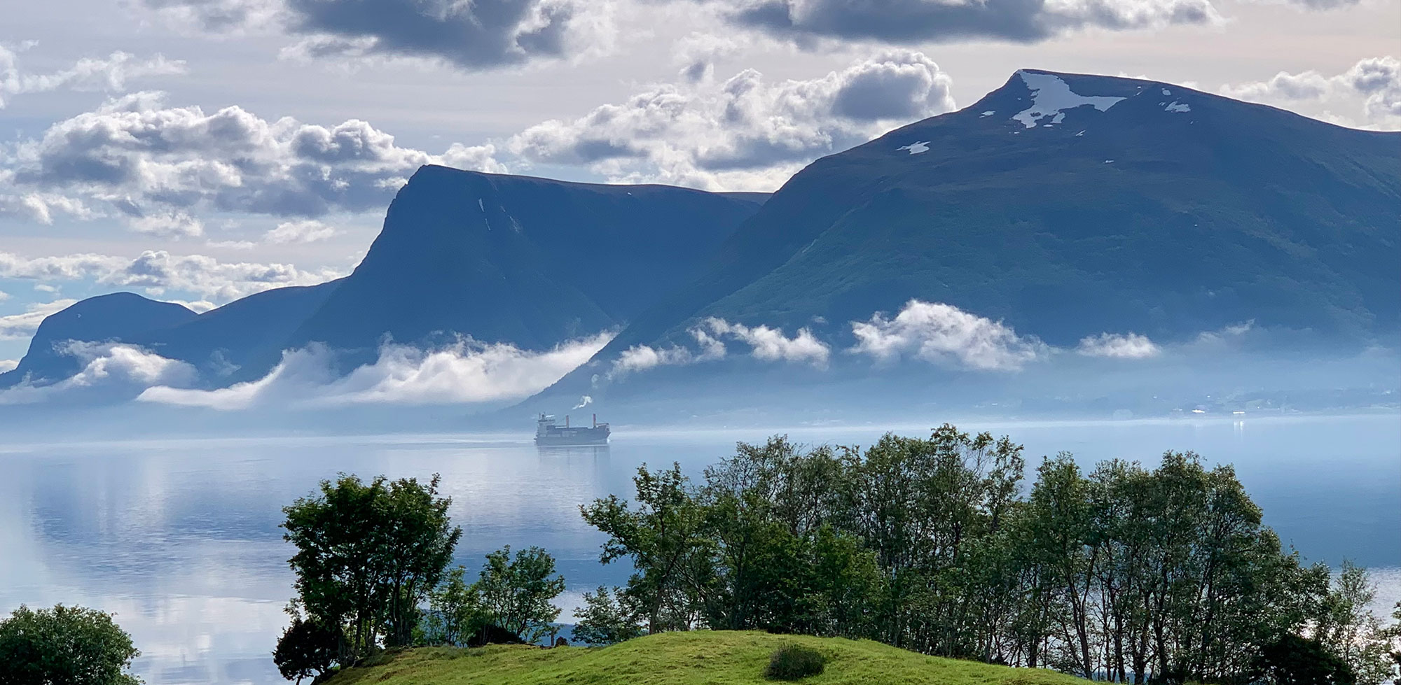 Dramatiske fjell omgitt av skyer, med dis som ligger over vannet under.