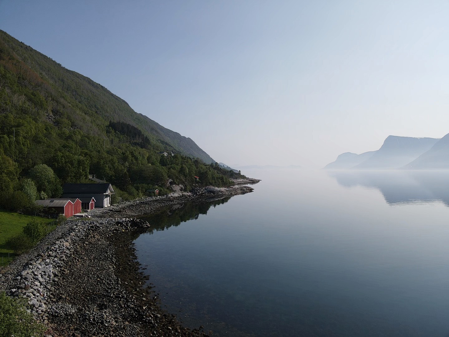 Strandsonen på Almestranda med blå sjø, blå himmel og lett dis som ligger over vannflaten.